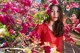 A woman in a red dress standing in front of a tree with pink flowers.