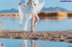 A woman in a white dress standing by a body of water.