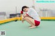 A woman in a white shirt and red shorts crouching on a green floor.