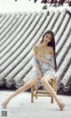 A woman sitting on a wooden chair in front of a roof.