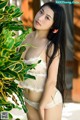 A woman in a white lingerie posing next to a plant.