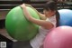 A woman sitting on top of a large green and pink ball.