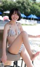 A woman in a bikini sitting on a chair by a pool.